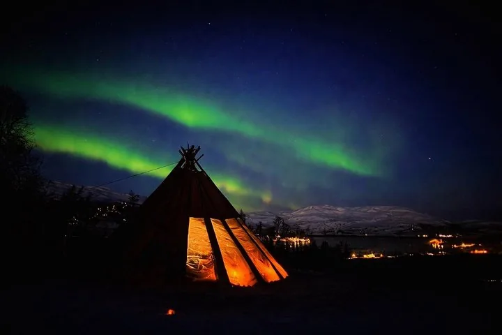 Une tente lavvo illuminée sous des aurores boréales vertes la nuit